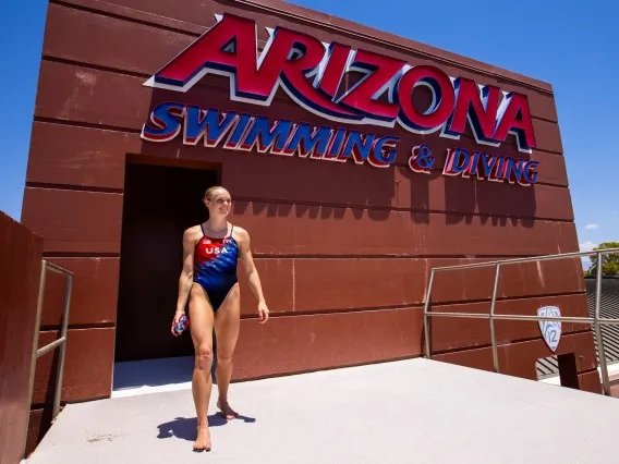 A woman in a blue and redcompetitive swimwear at the top of a diving platform. Above her are the words "Arizona Swimming & Diving"