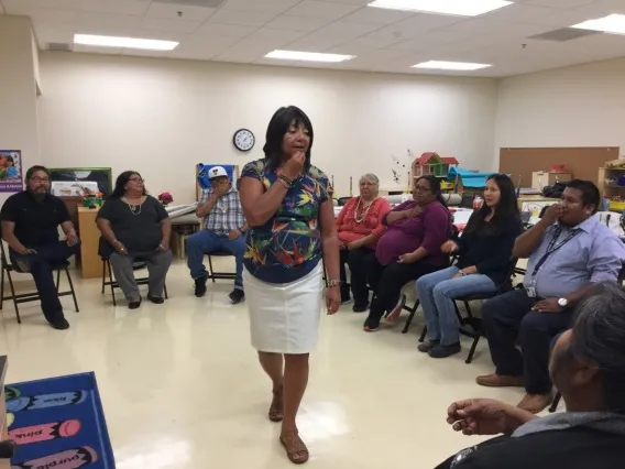 Sheilah Nicholas standing and gesturing during a lecture in front of an audience circled around her in a classroom