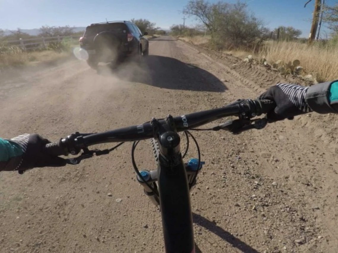 a first-person view of someone riding a bicycle, with arms extending to handlebars while riding down a dusty dirt road