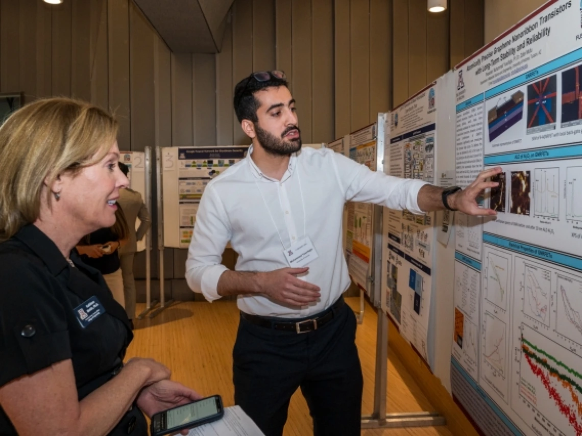 Muhammed Yusufoglu gesturing toward a poster while another person looks on